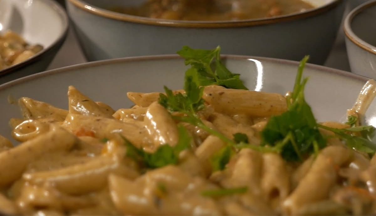 Rasta Pasta dish with creamy sauce, garnished with fresh herbs, in a ceramic bowl.