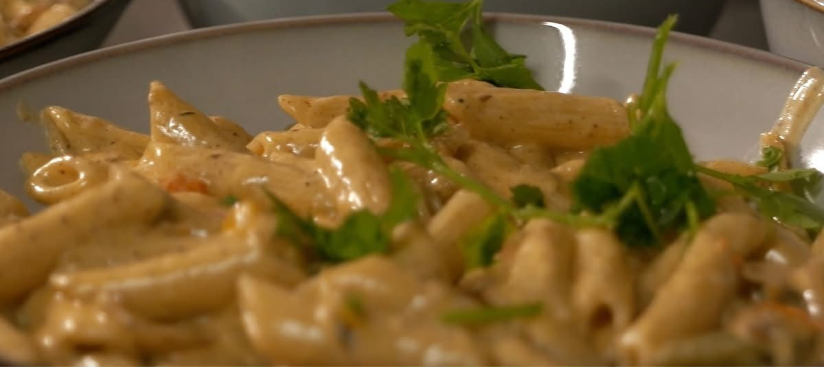 Penne Rasta pasta in a creamy sauce, garnished with fresh herbs, in a ceramic bowl.