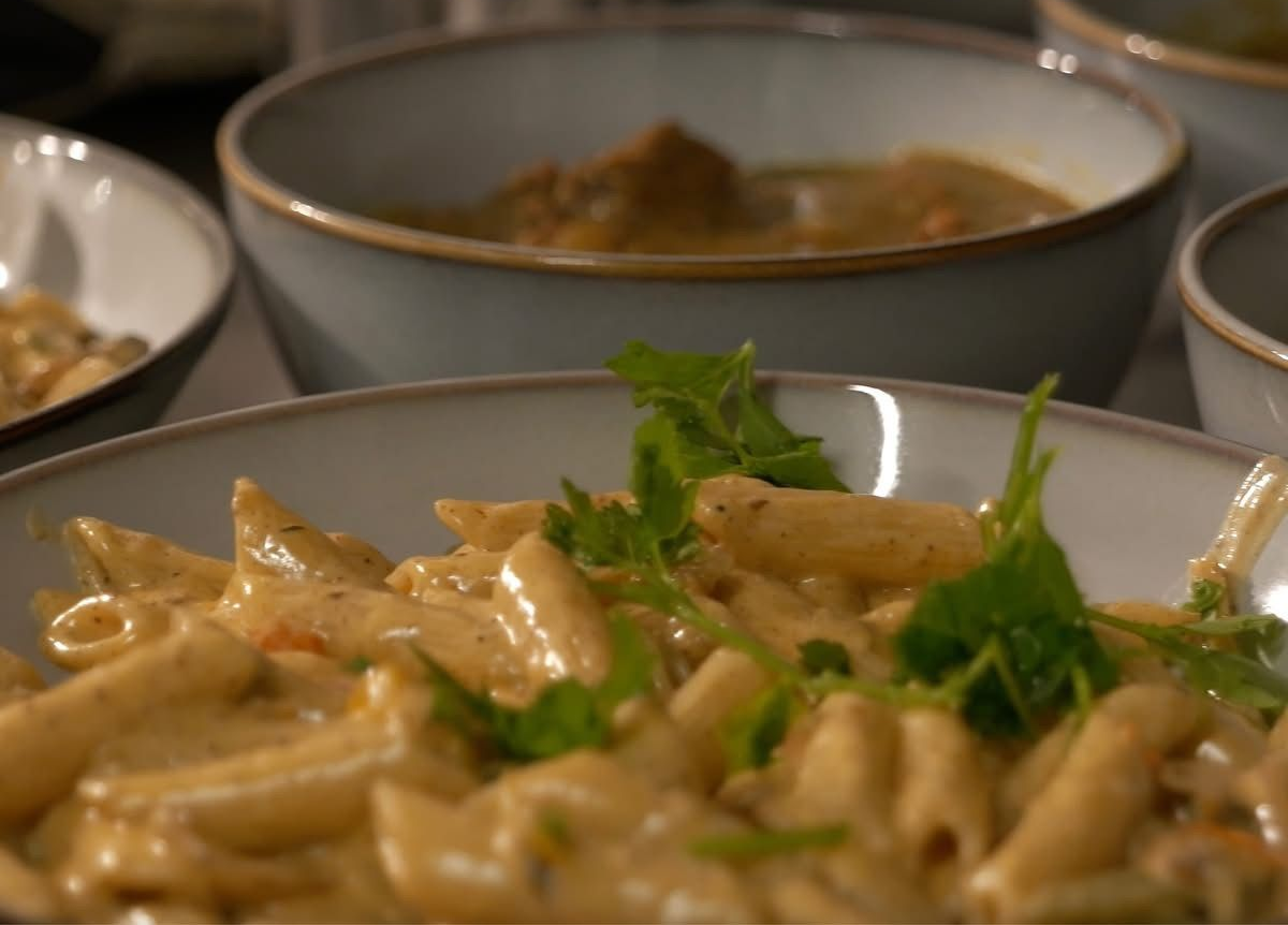 Close-up of creamy penne Rasta pasta in a bowl, with other bowls of food in the background.