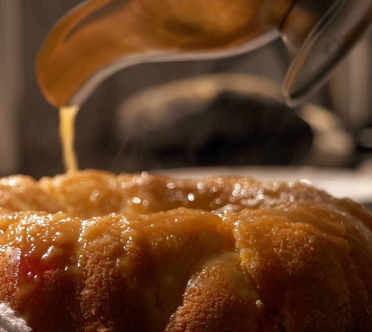 Pineapple Rum Cake being drizzled with a golden syrup. Close-up with focus on cake, steam rising, warm tones.