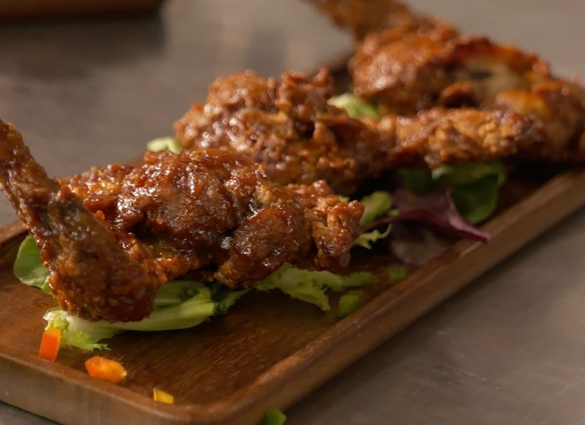 Fried chicken wings with glossy sauce on a bed of salad, served on a wooden platter.