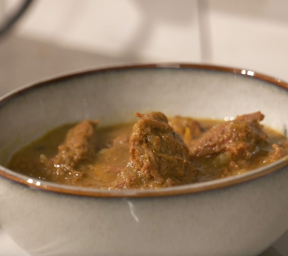 Bowl of curried goat with chunks of meat.