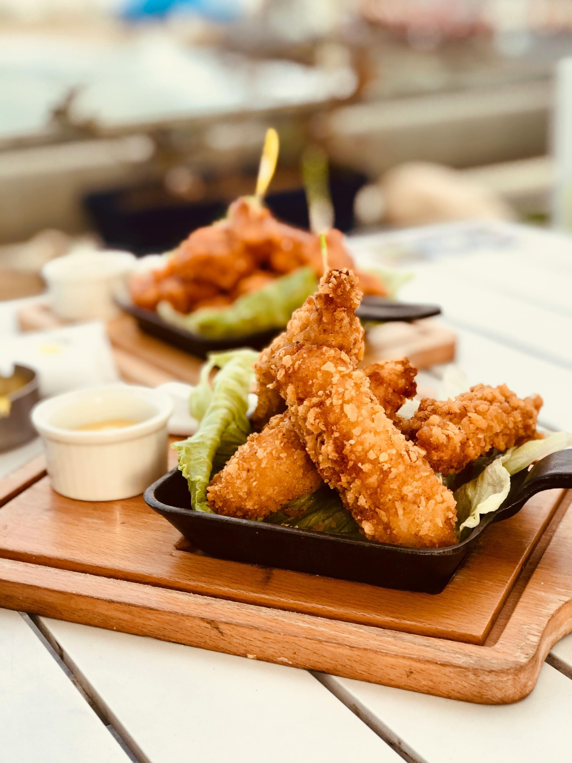 Crispy fried chicken tenders with dipping sauce, on a wooden board.