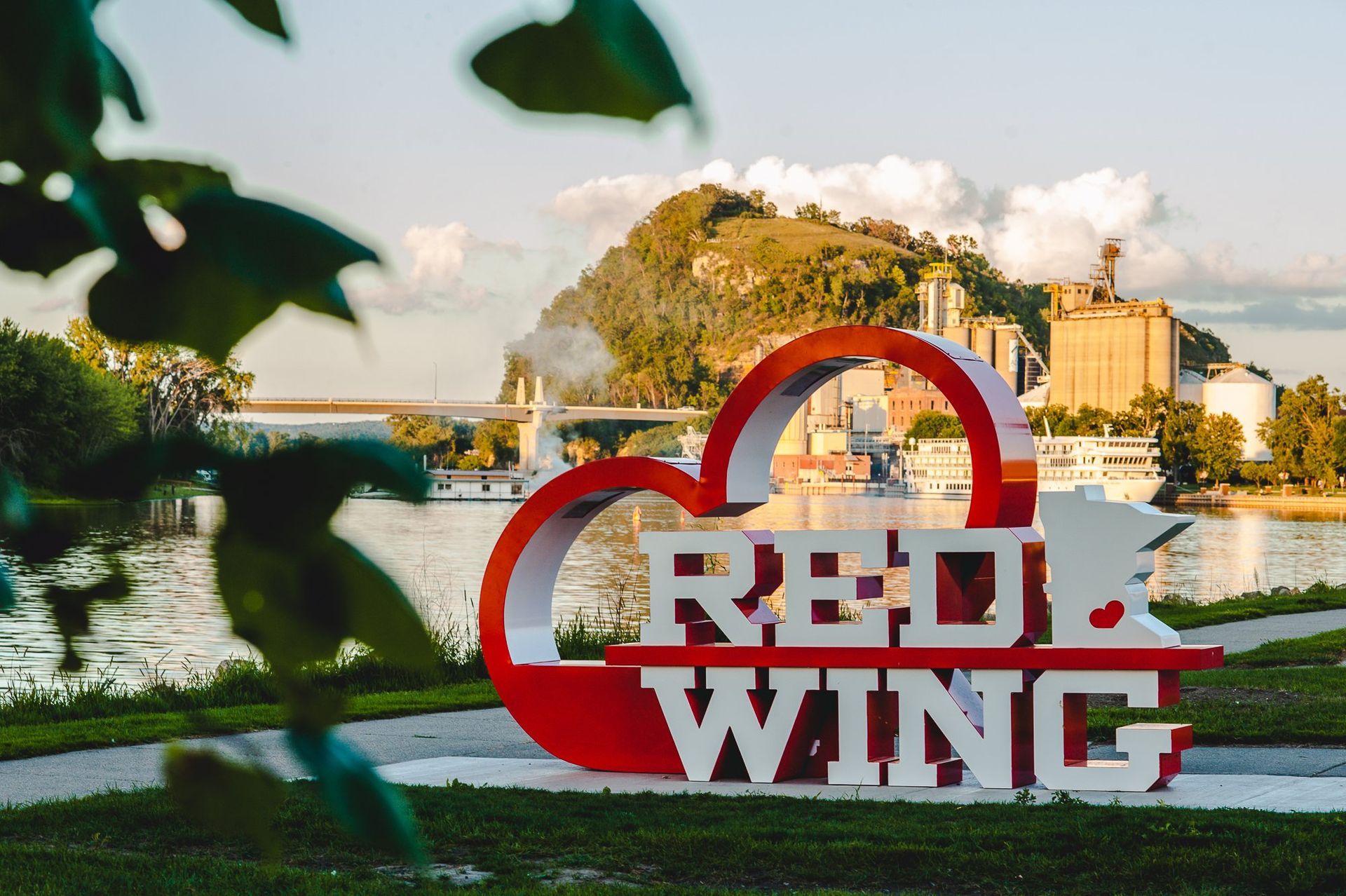 A red and white sign that says red wing in front of a river.
