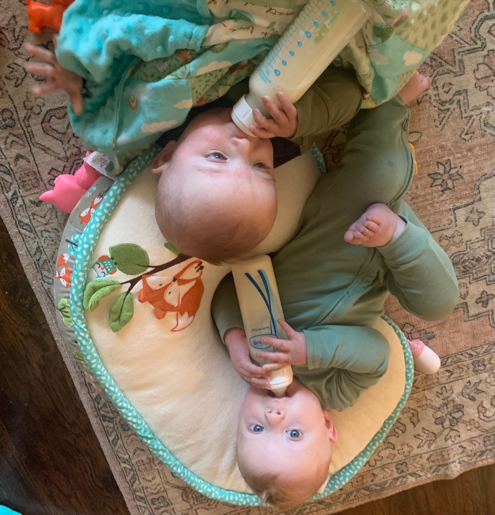 Two babies are laying on a pillow drinking from bottles.