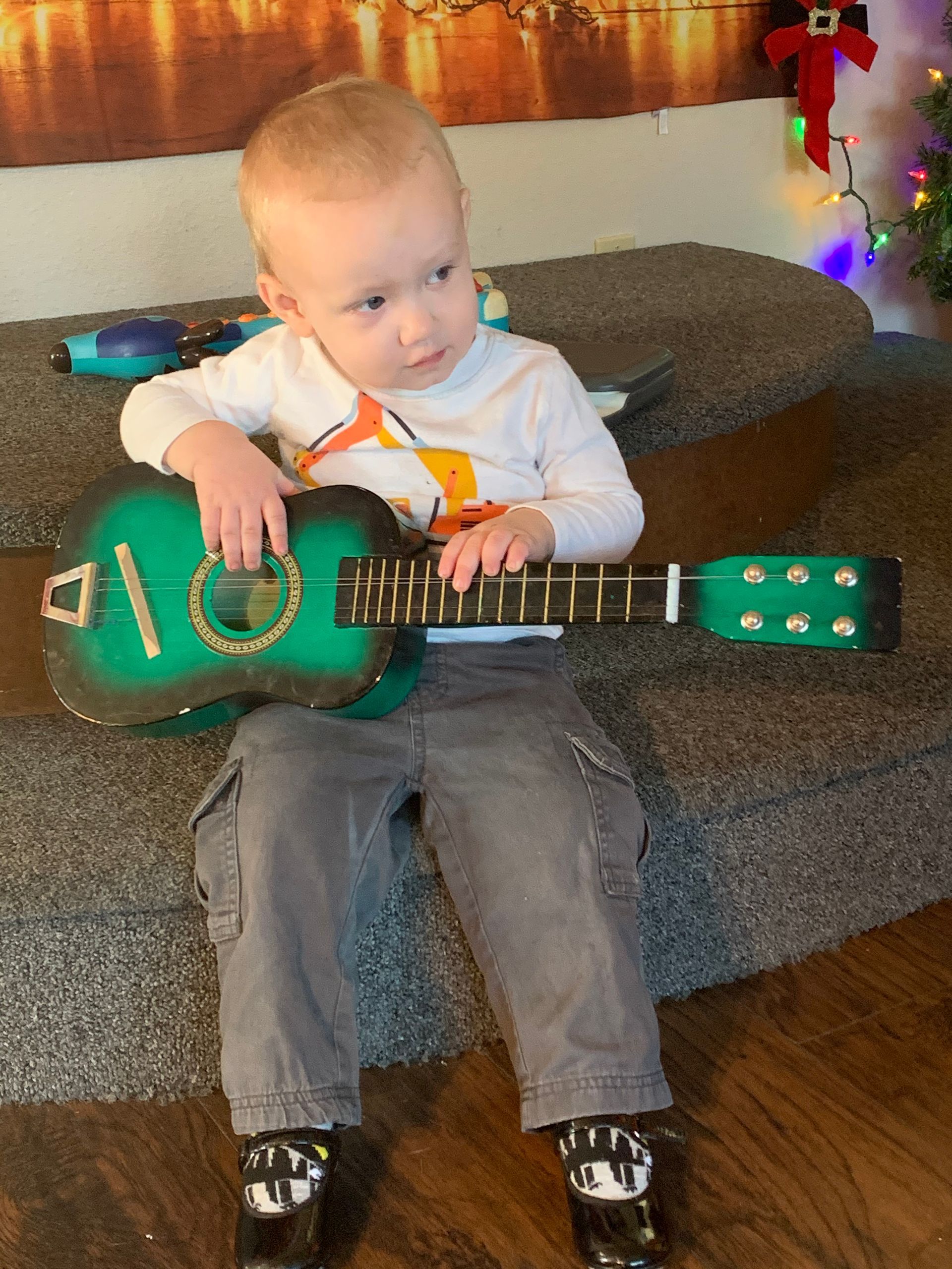 A little boy is sitting on a couch playing a guitar