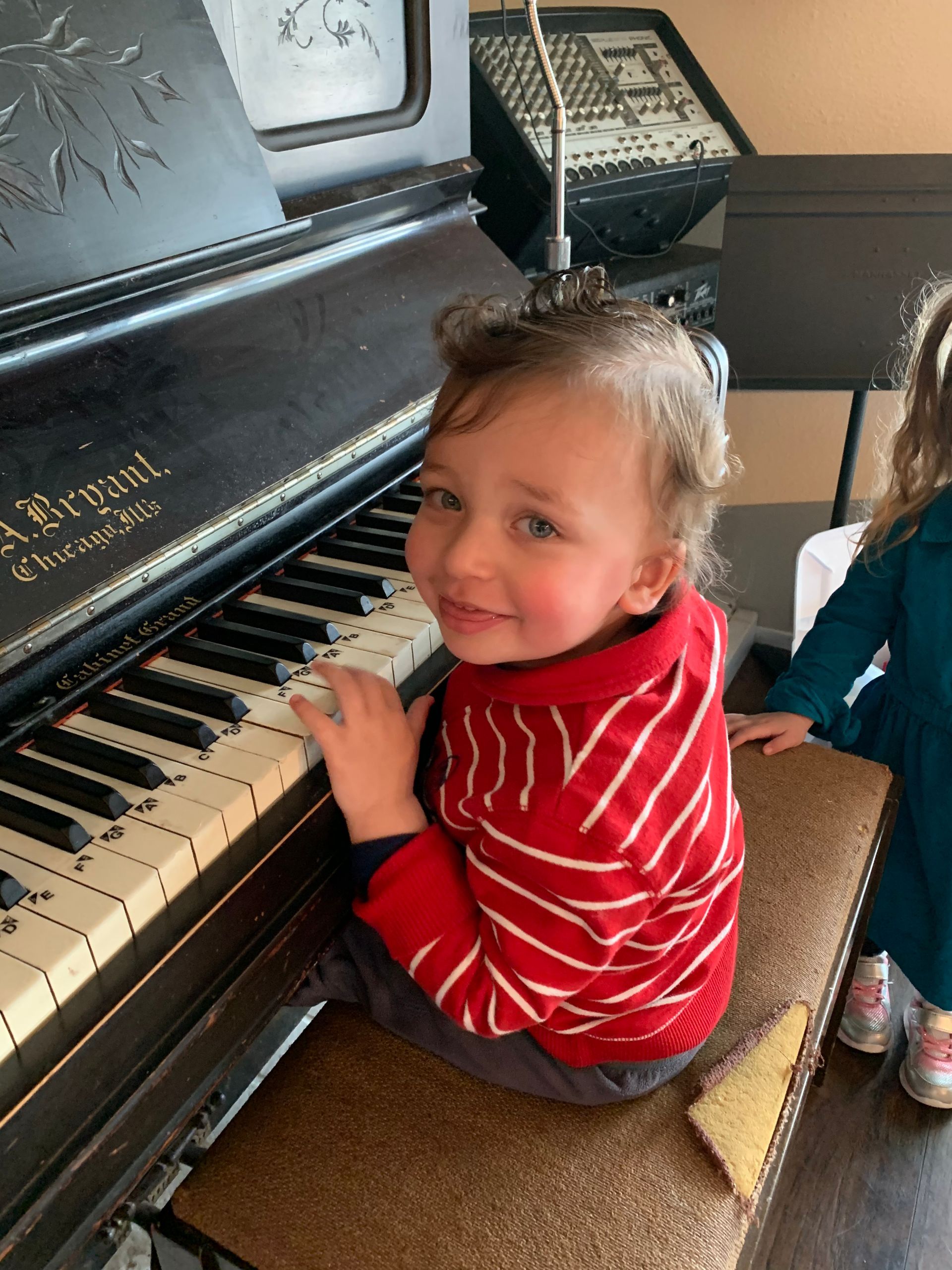 A little girl in a red and white striped shirt is playing a piano