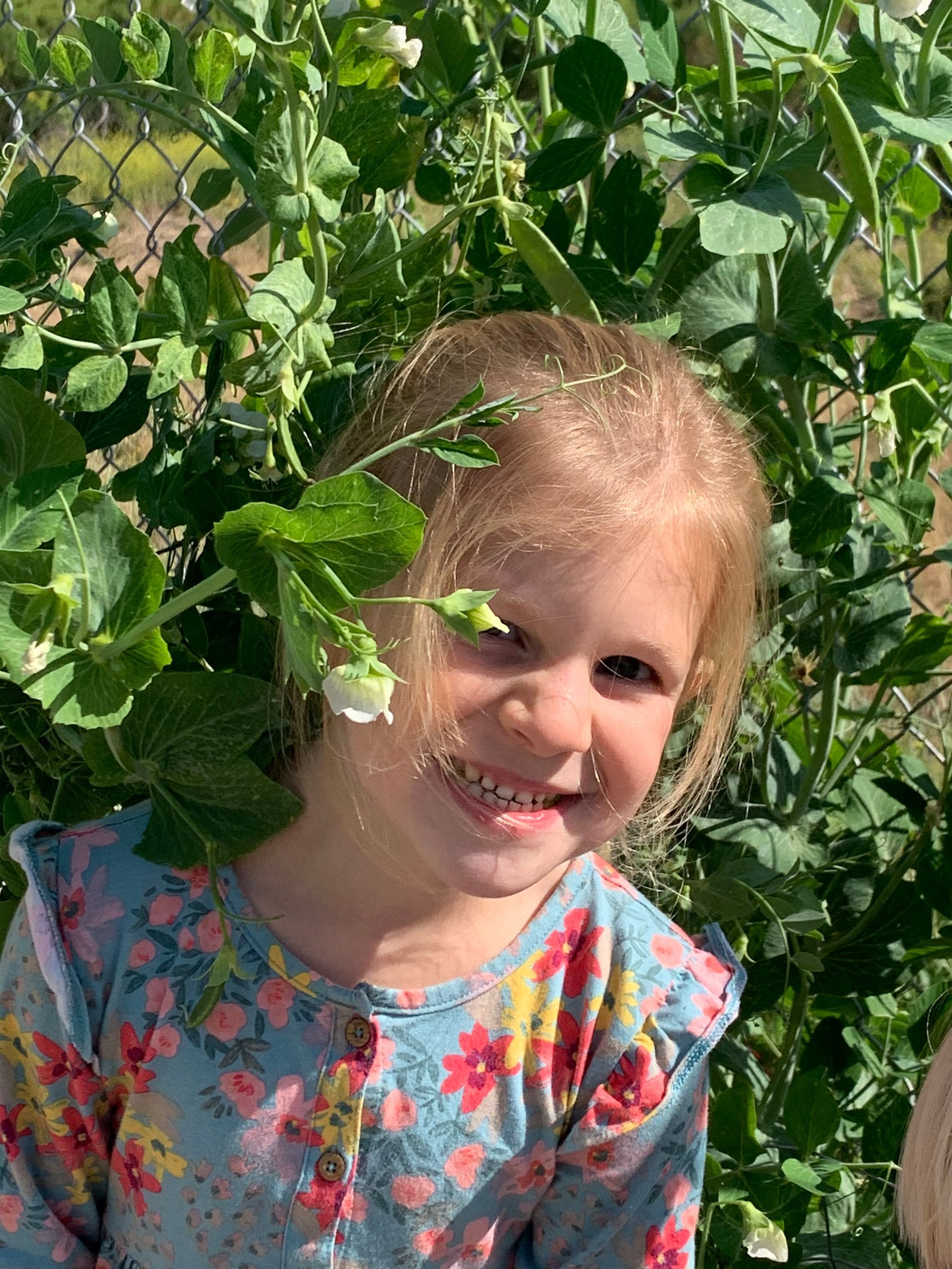 A little girl is smiling while standing in a garden surrounded by plants.