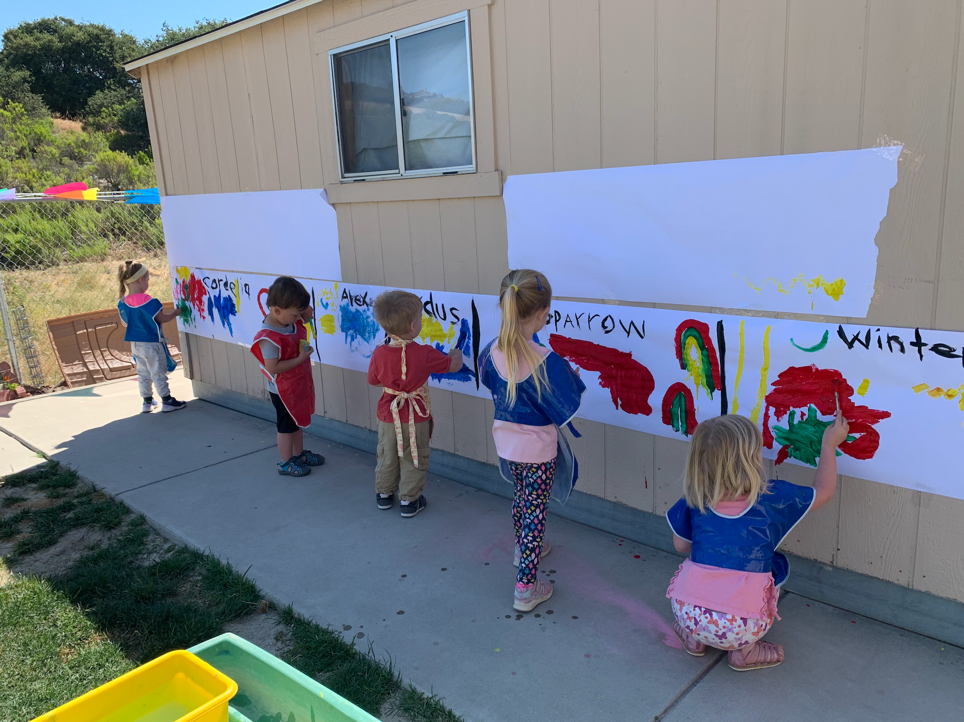 A group of children are painting on a wall.