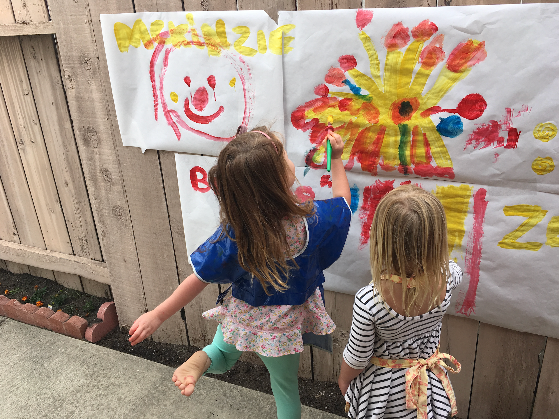 Two little girls are painting on a large piece of paper.