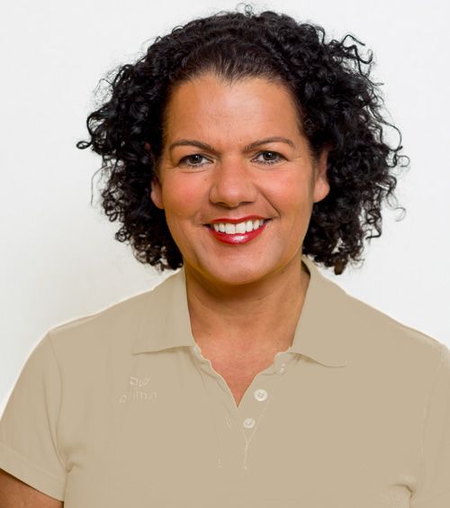 Zahnärztin Christina Lippmann mit lockigem Haar lächelt und trägt ein hellbraunes Poloshirt