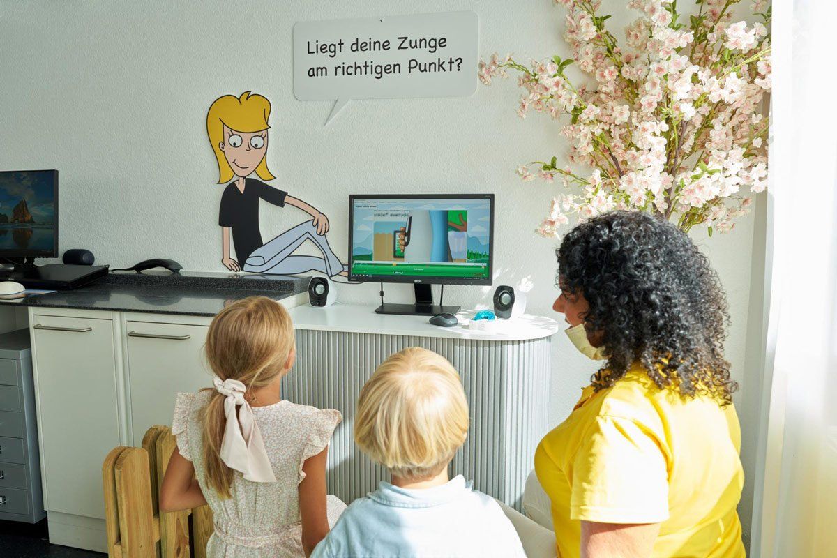 Zahnärztin Christina Lippmann und zwei Kinder schauen auf einen Computerbildschirm.