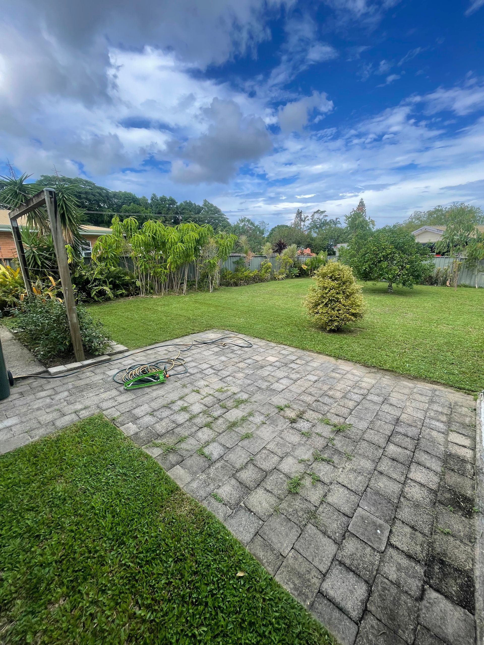 Backyard with Brick Patio, Green Grass, Garden, Trees, and Cloudy Blue Sky — Lads Lawns & Gardens in Bentley Park, QLD