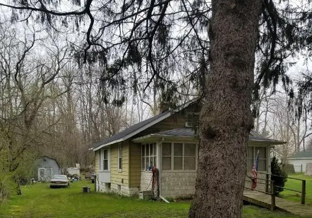 Yellow house with screen porch and wooden walkway, set in a yard with a large tree in the foreground.