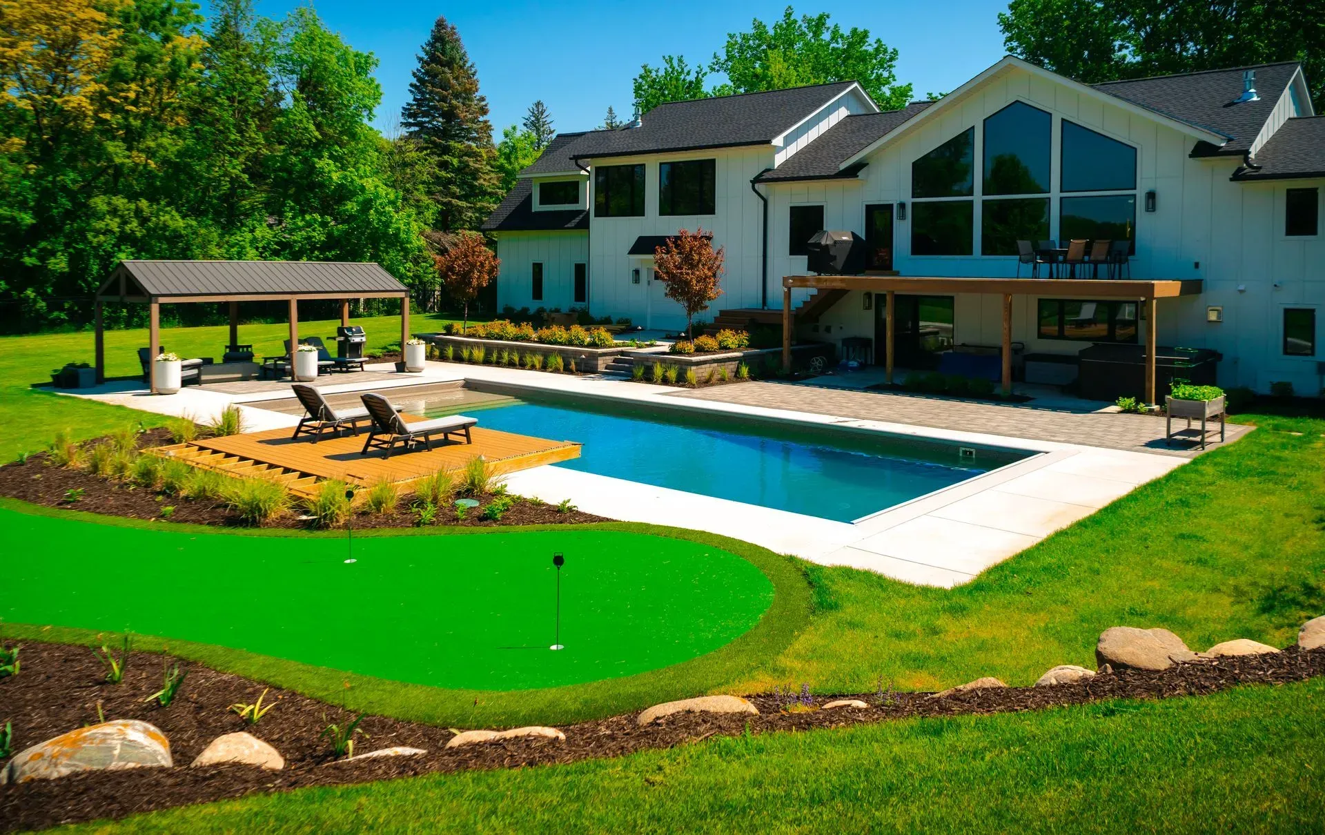Modern landscape design blending pool, garden, shaded lounge, and putting green.
