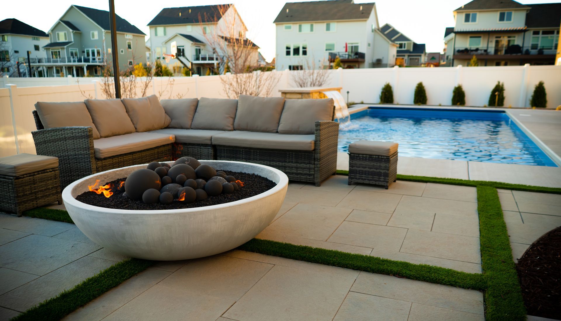 Modern patio with sectional sofa, fire pit bowl, and swimming pool in a suburban backyard