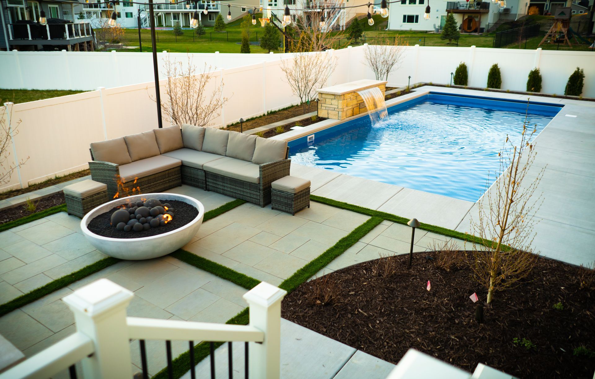Patio with sectional seating, fire pit, and a blue swimming pool beside a white fence