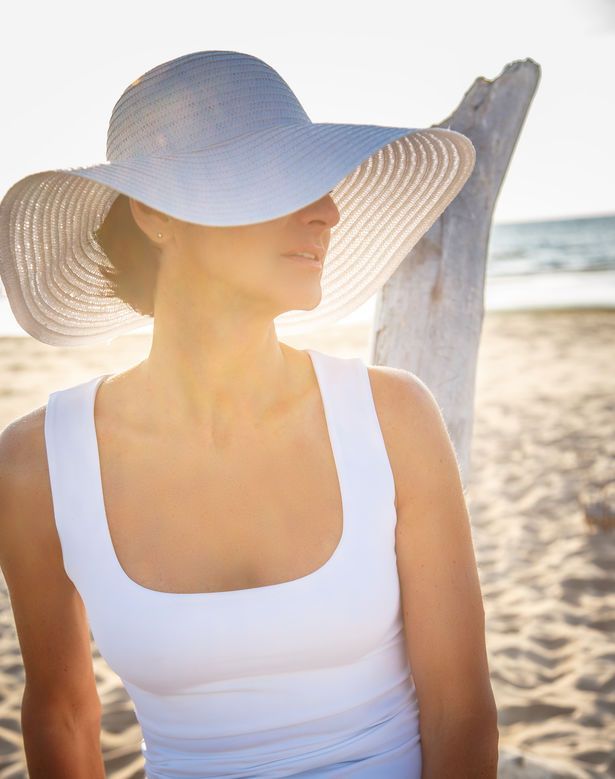 A woman wearing a white hat is standing on the beach