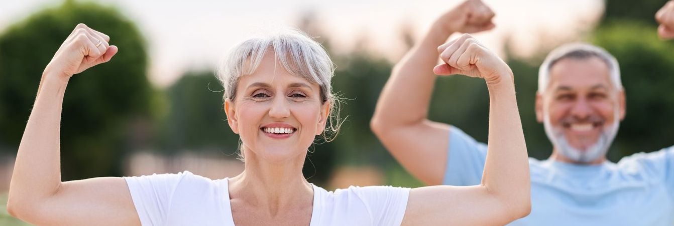 A man and a woman are flexing their muscles in a park.