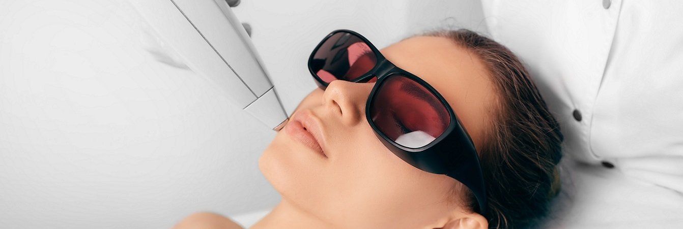 A woman wearing sunglasses is getting a laser treatment on her face.