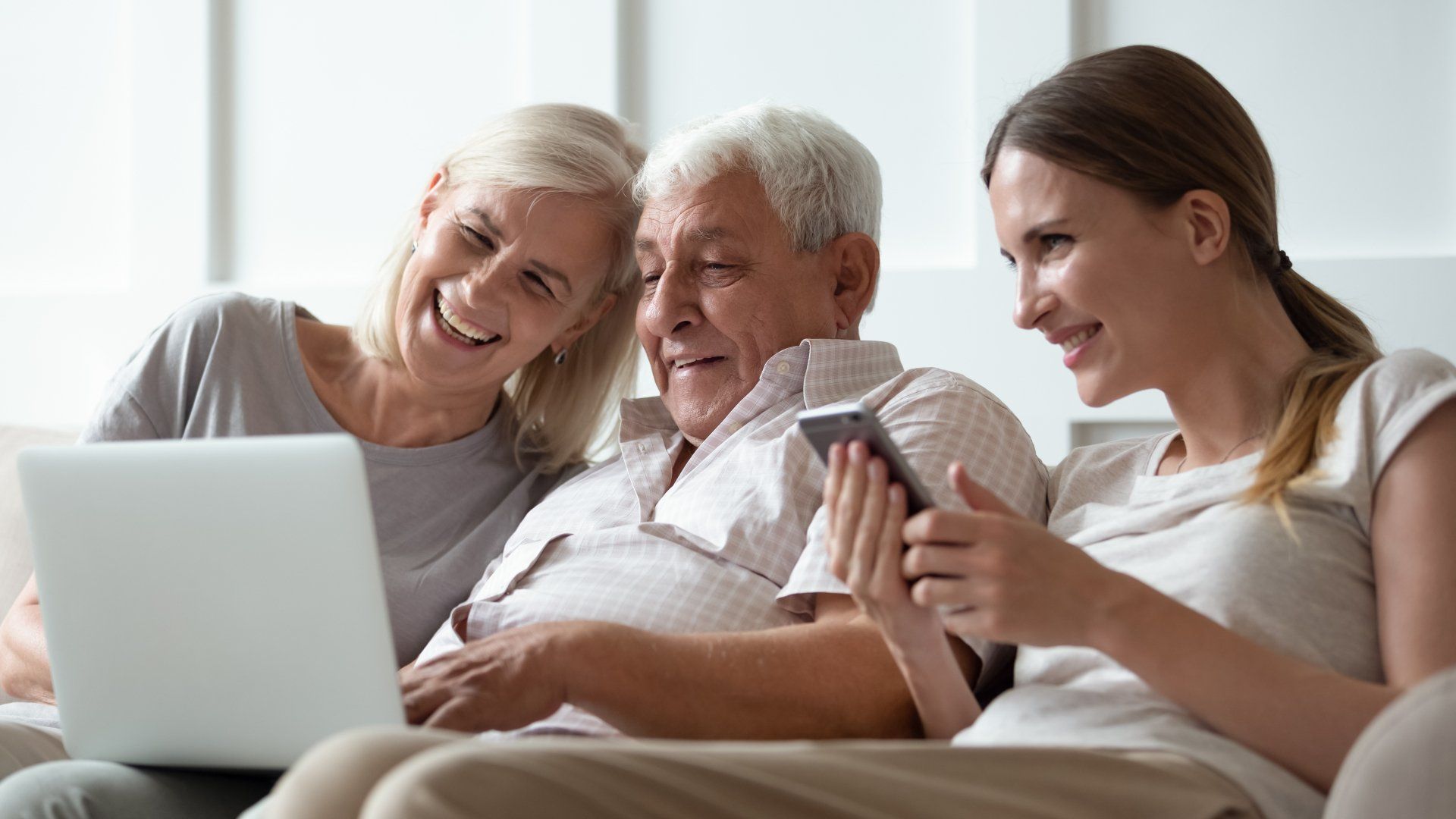 A family is sitting on a couch looking at a laptop and a cell phone.