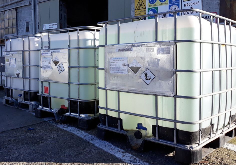 Tre grandi contenitori trasparenti per lo stoccaggio di sostanze chimiche disposti in fila, con etichette di pericolo.