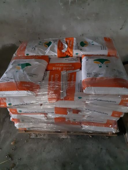 Pallet di acido citrico in sacchi, avvolto in plastica trasparente. Sacchi arancioni e bianchi impilati su pallet di legno.