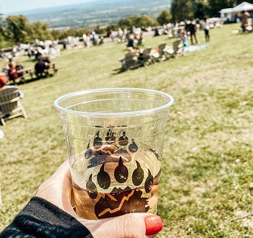 A person is holding a cup of beer in a field.
