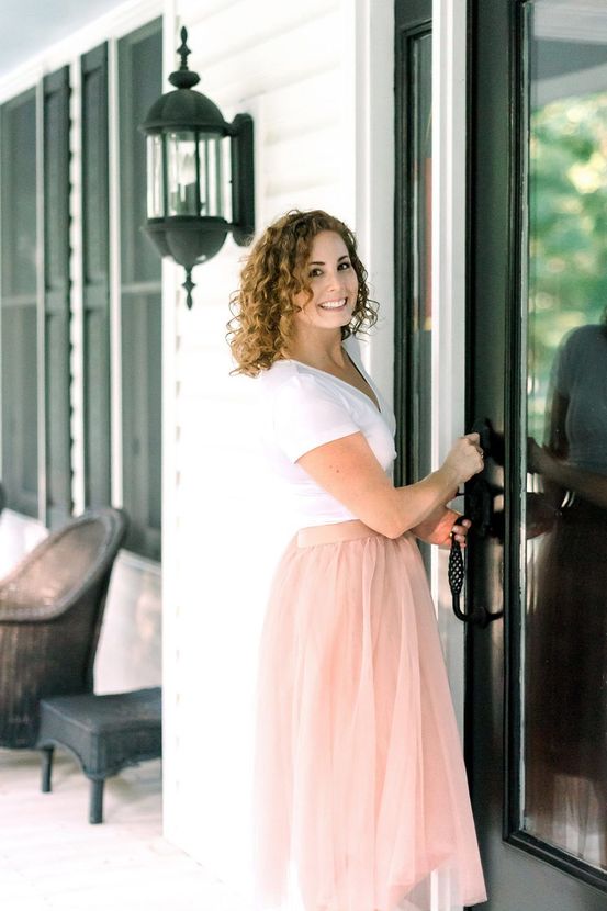 A woman in a pink tulle skirt is standing in front of a screened in porch. A woman in a pink tulle skirt is standing in front of a screened in porch.
