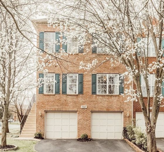 A large brick house with two garages and trees in front of it.