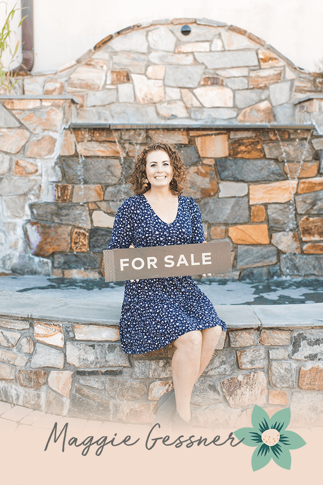 A woman is sitting on a stone wall holding a for sale sign. A woman is sitting on a stone wall holding a for sale sign.