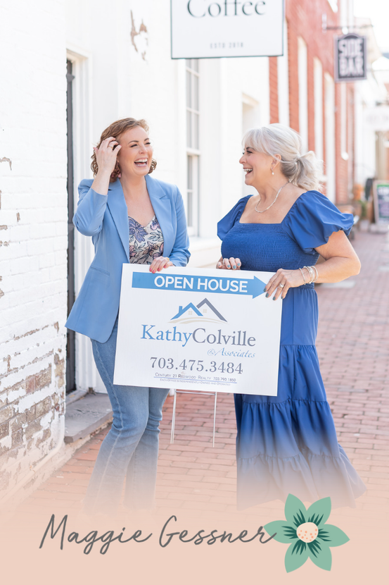 Two women are holding an open house sign in front of a building.