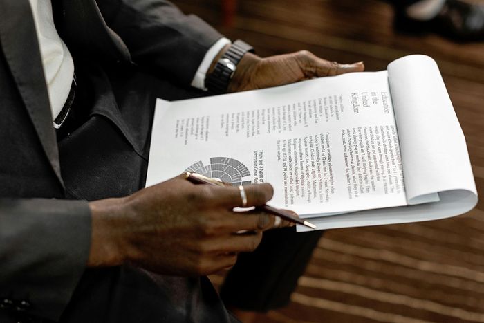 A person in a suit holds a pen and a document with text and a circular chart.
