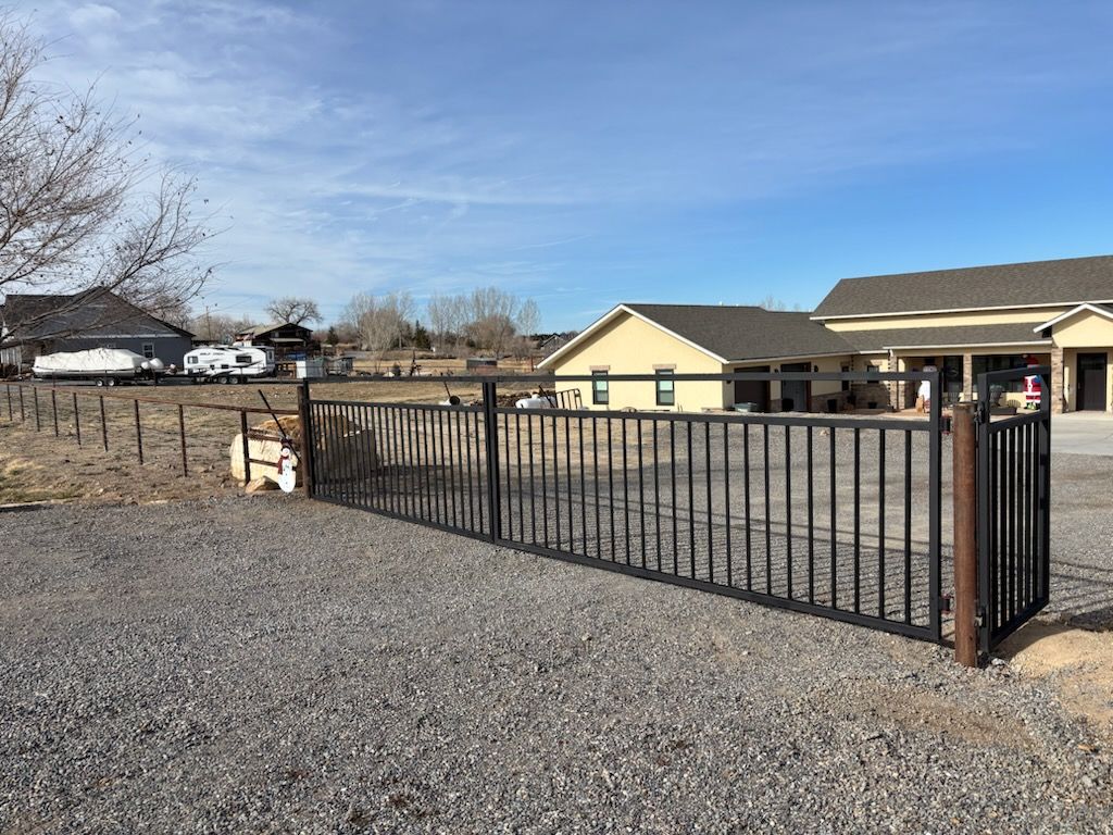 Black metal gate in gravel driveway beside a beige ranch house under a clear blue sky