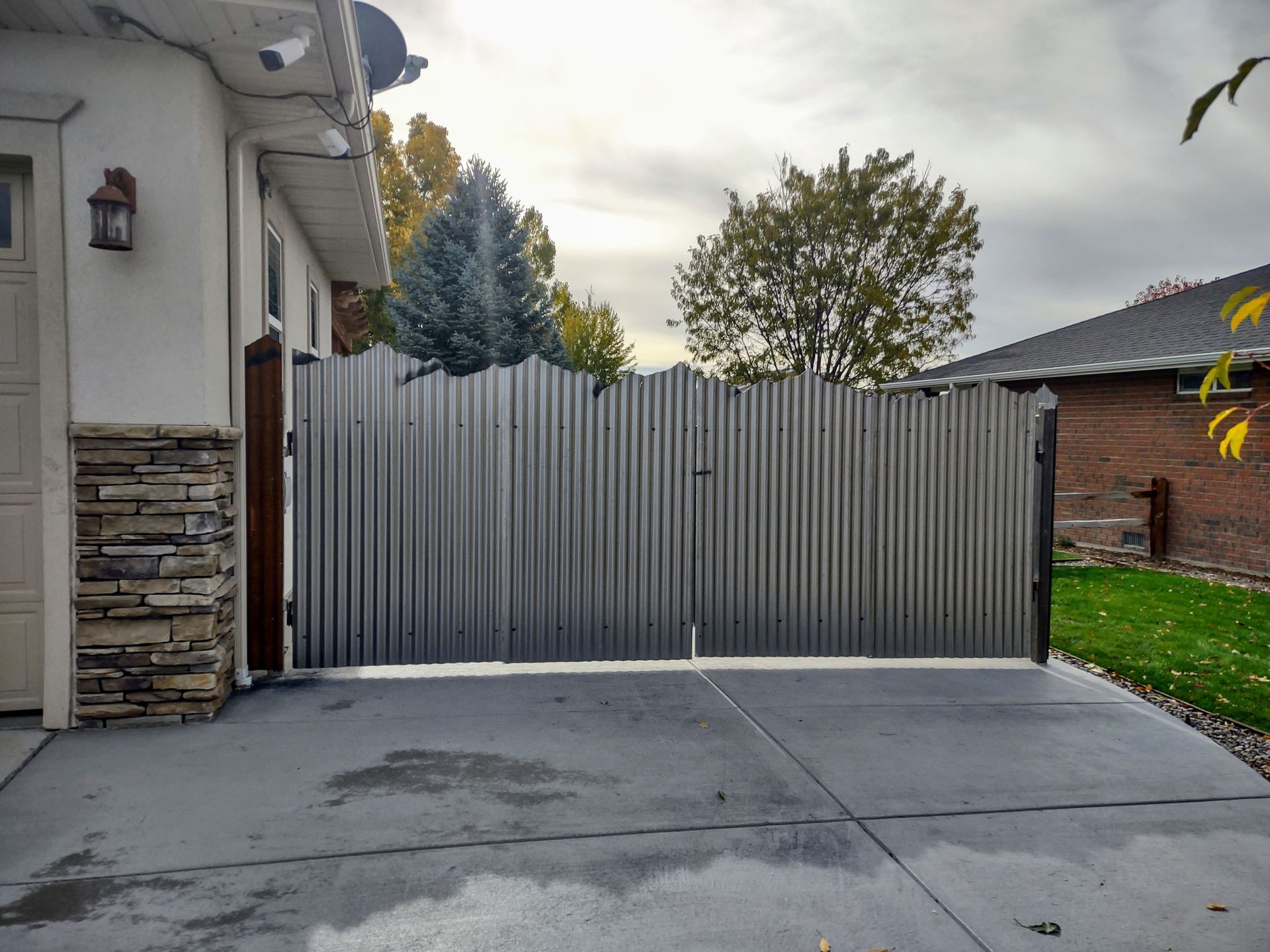 Gray metal gate across a driveway beside a white house and a lawn