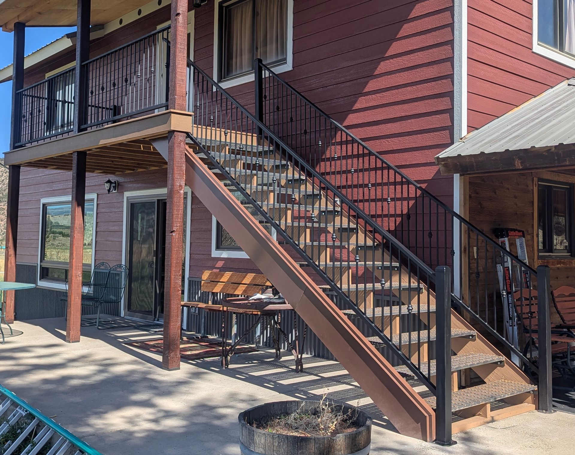 Outdoor staircase beside a red-sided two-story building with a shaded patio and table below
