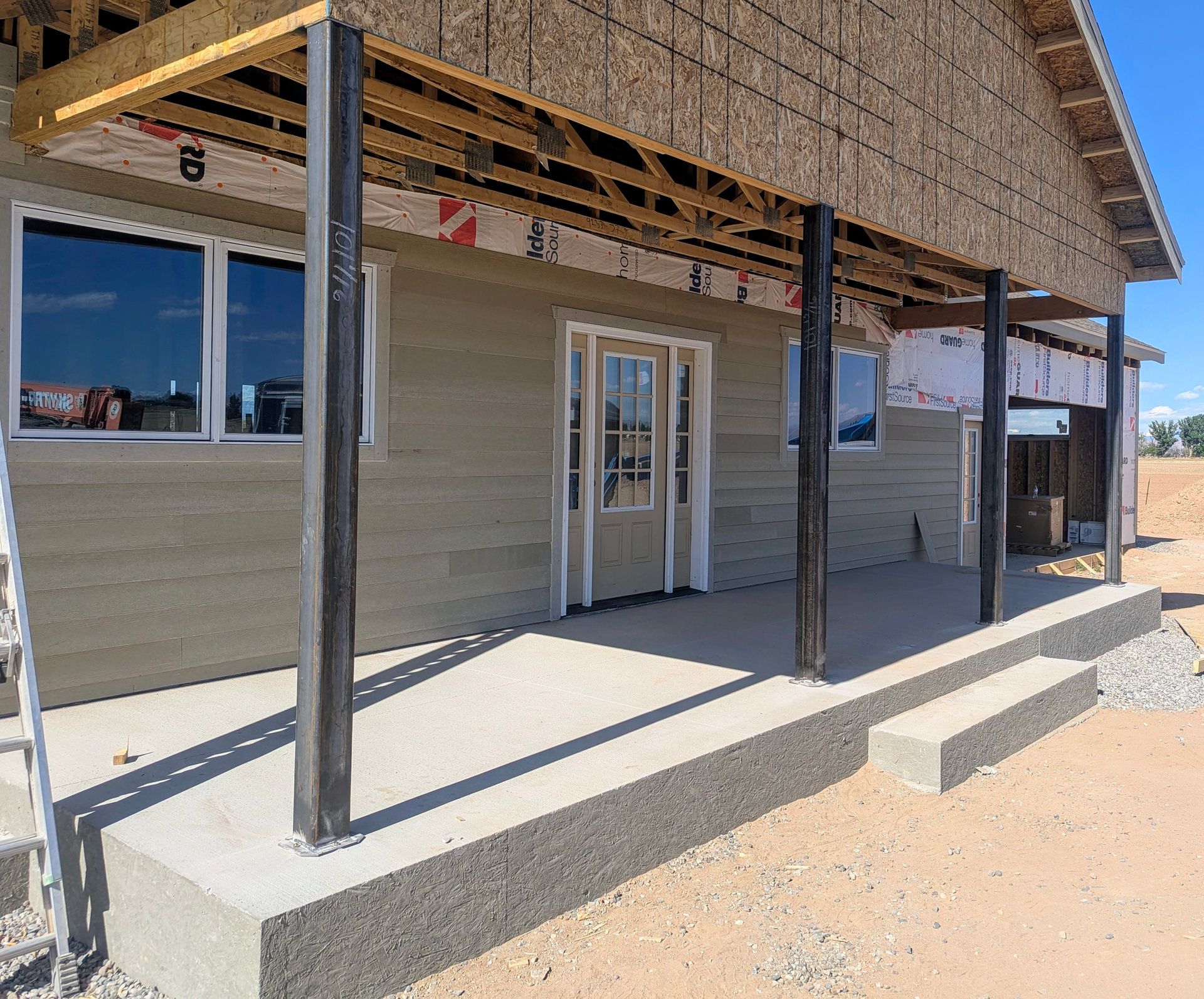 Small storefront porch with black posts, gray siding, and a central glass door under construction.