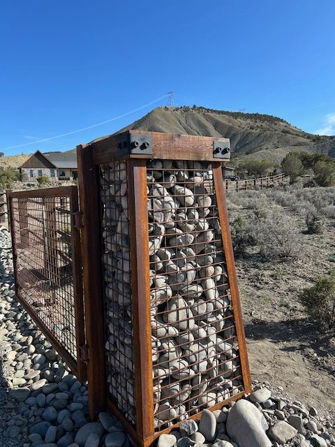 Gabion fence post filled with rocks beside a chain-link fence in a dry desert landscape
