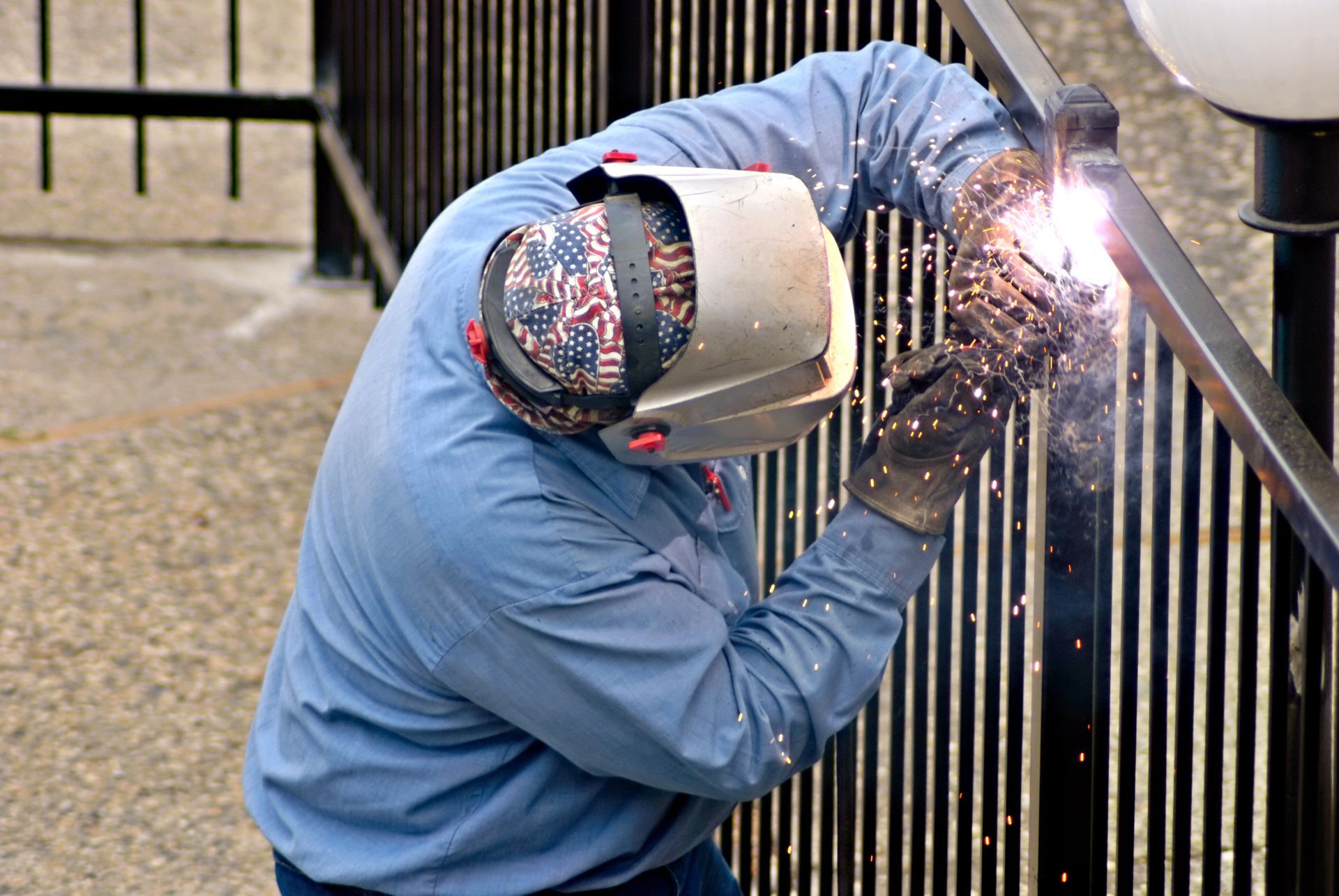 Worker welding a black metal railing, with bright sparks flying outdoors.