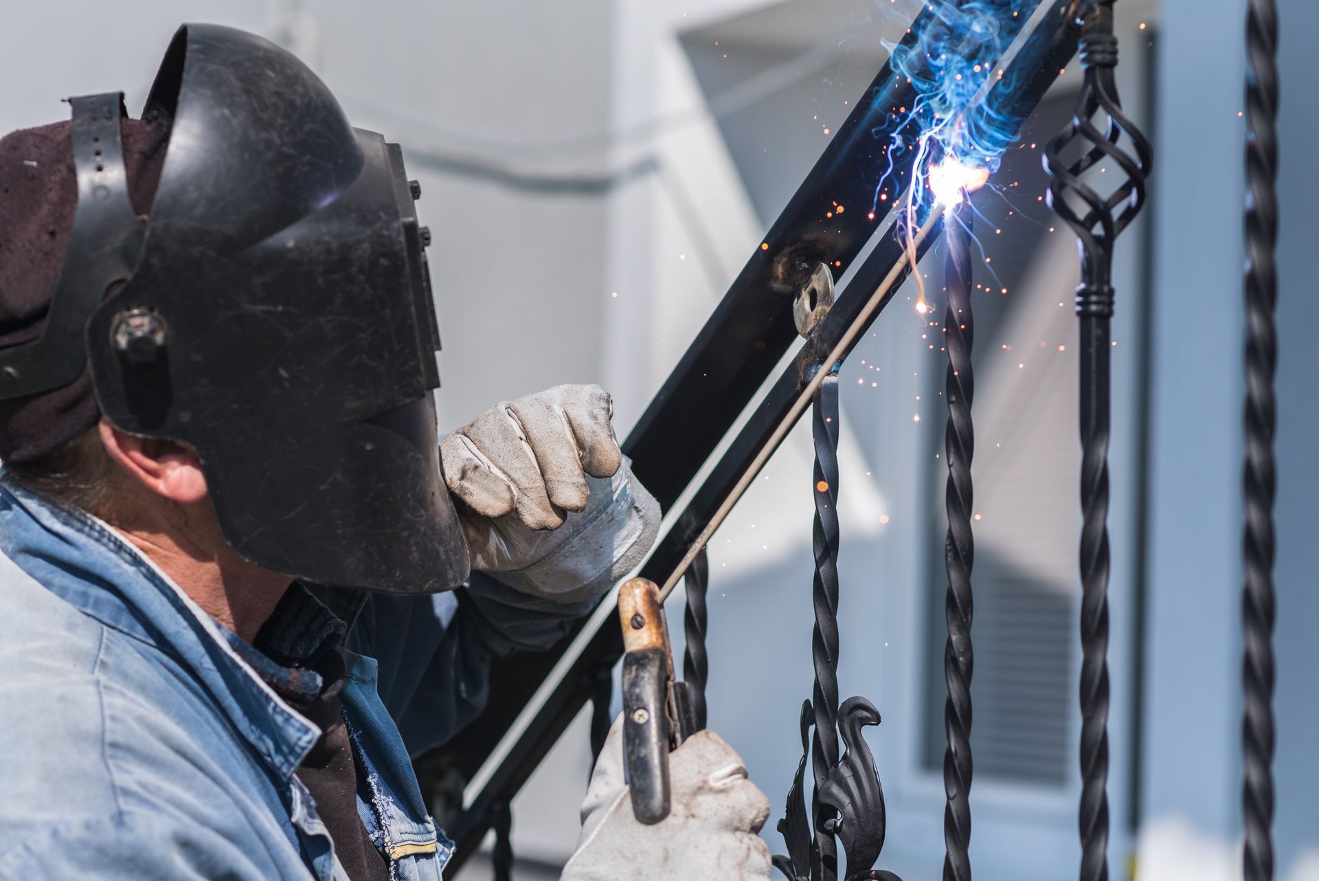 Welder in a face shield welding a metal frame, with bright sparks in an industrial setting