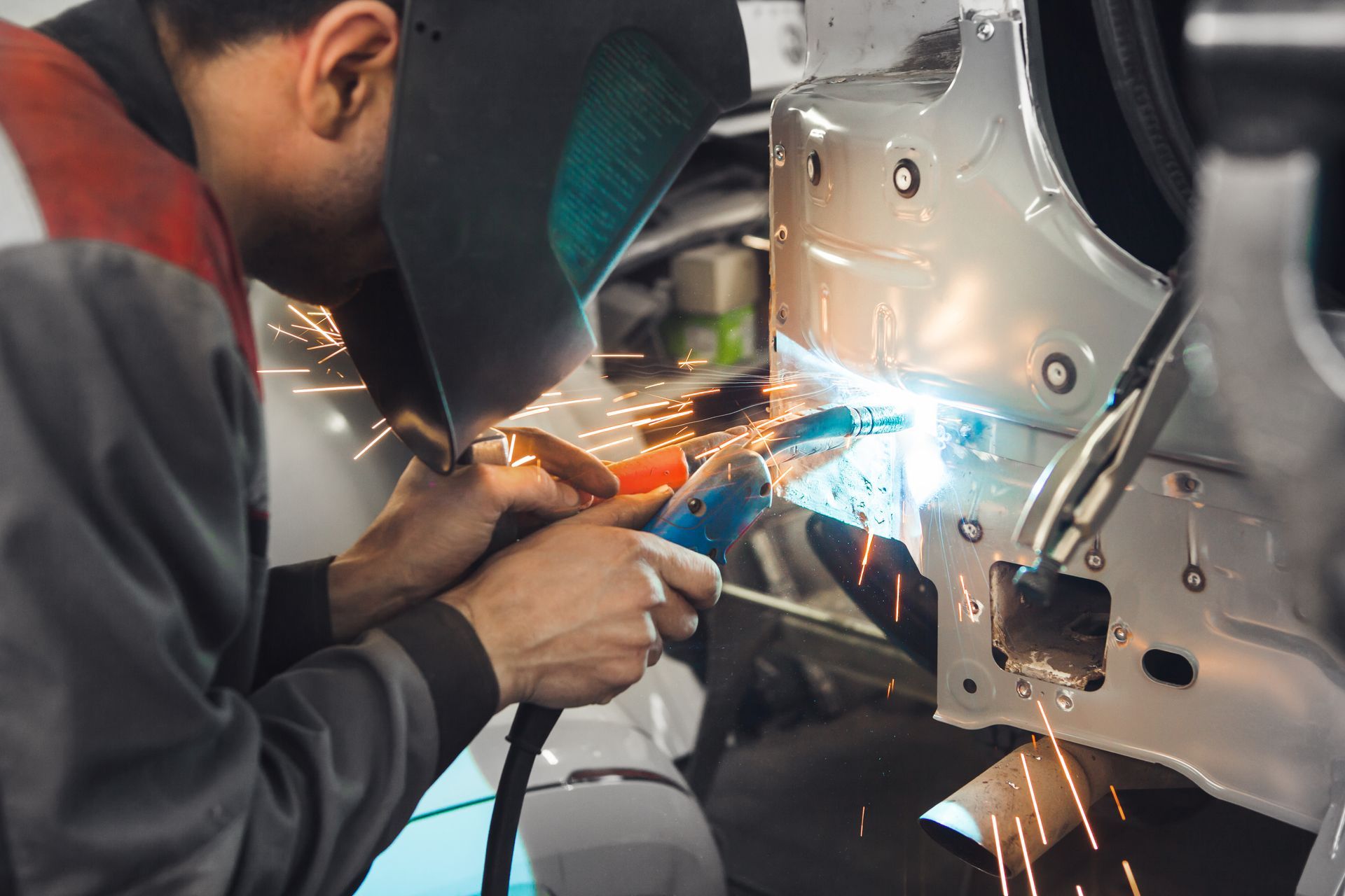 Worker welding metal on a car frame, with bright sparks in an auto repair shop