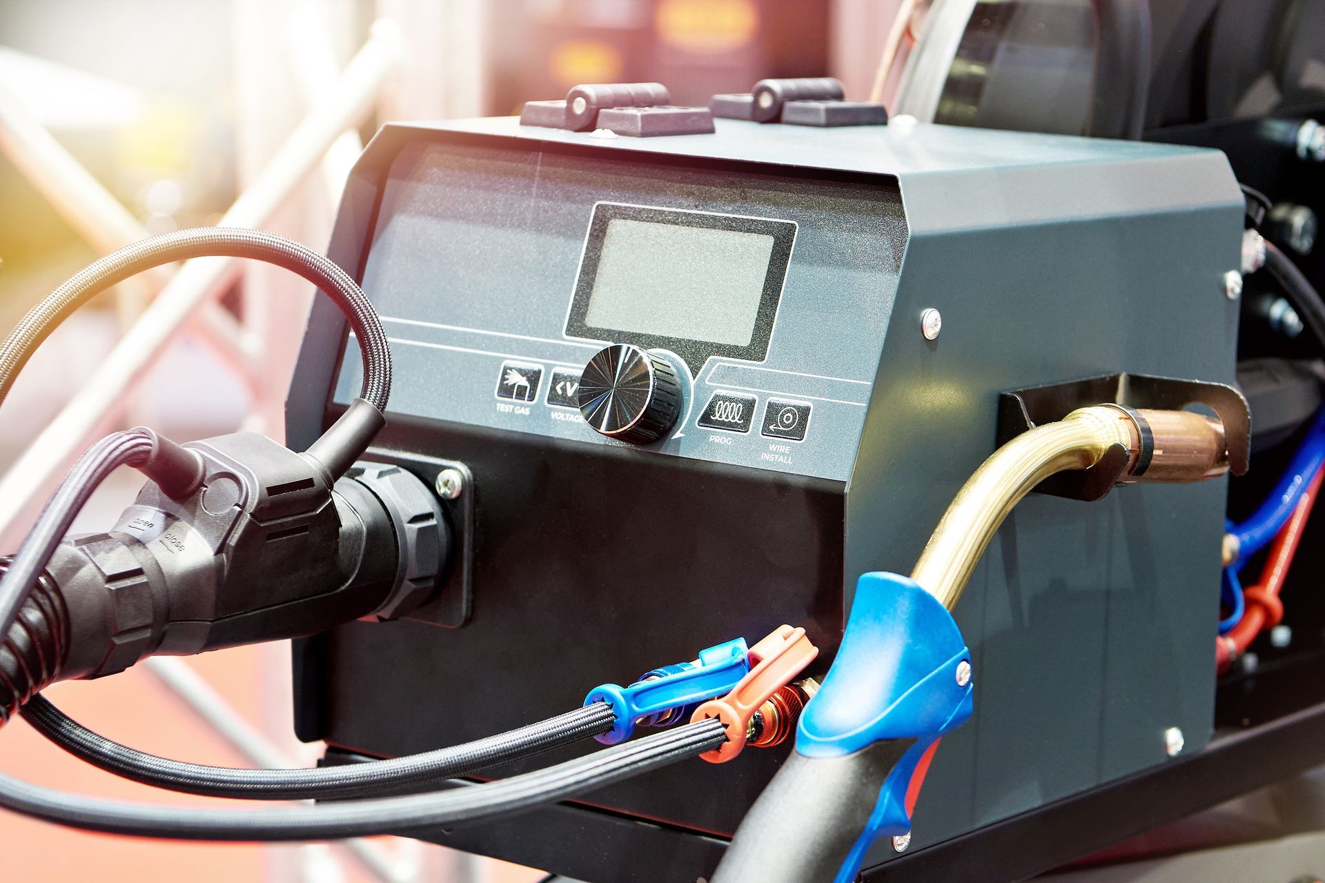 Close-up of a gray electronic device with cables and connectors on a workbench, lit by warm light