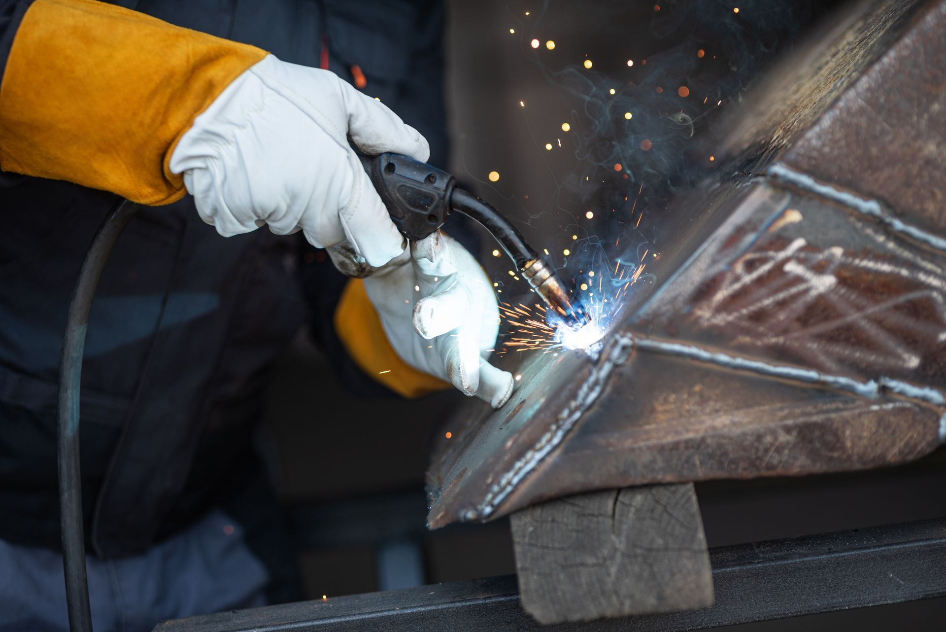 Gloved worker grinding metal, sending sparks from a steel surface