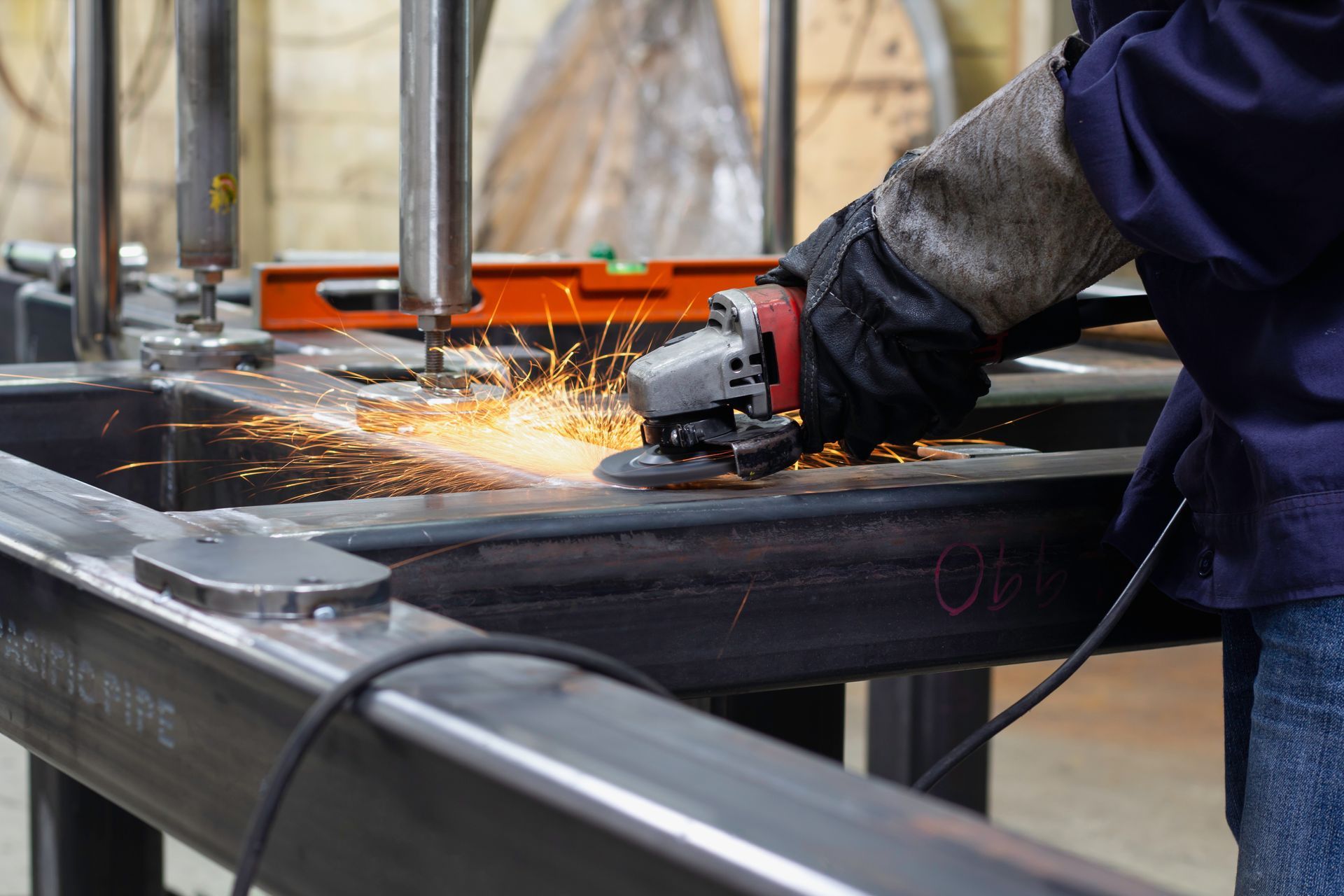Worker grinding metal on a steel workbench, sending sparks across an industrial shop floor