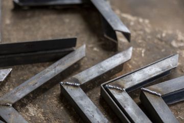 Metal angle brackets and steel strips scattered on a workshop floor with dust and debris