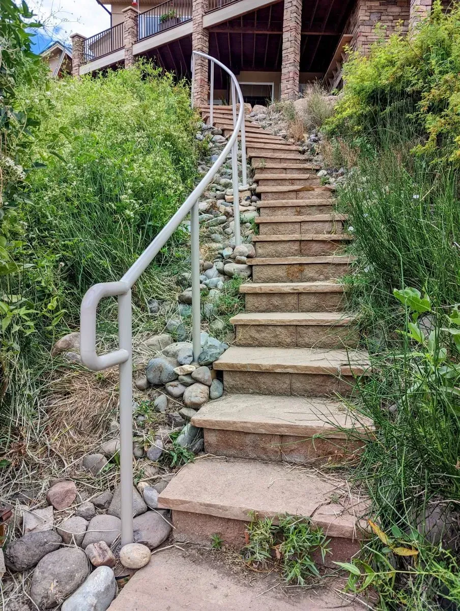 Steep outdoor stone staircase with metal handrail climbing a hillside beside a rustic building.