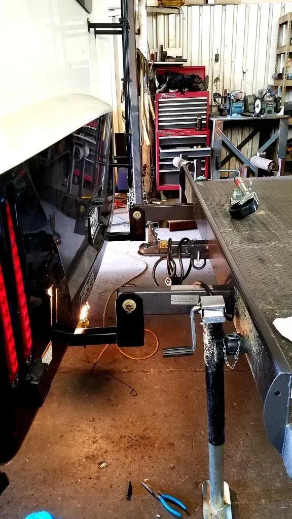 Narrow garage workspace with tools, a workbench, and a vehicle lift beside a black car.