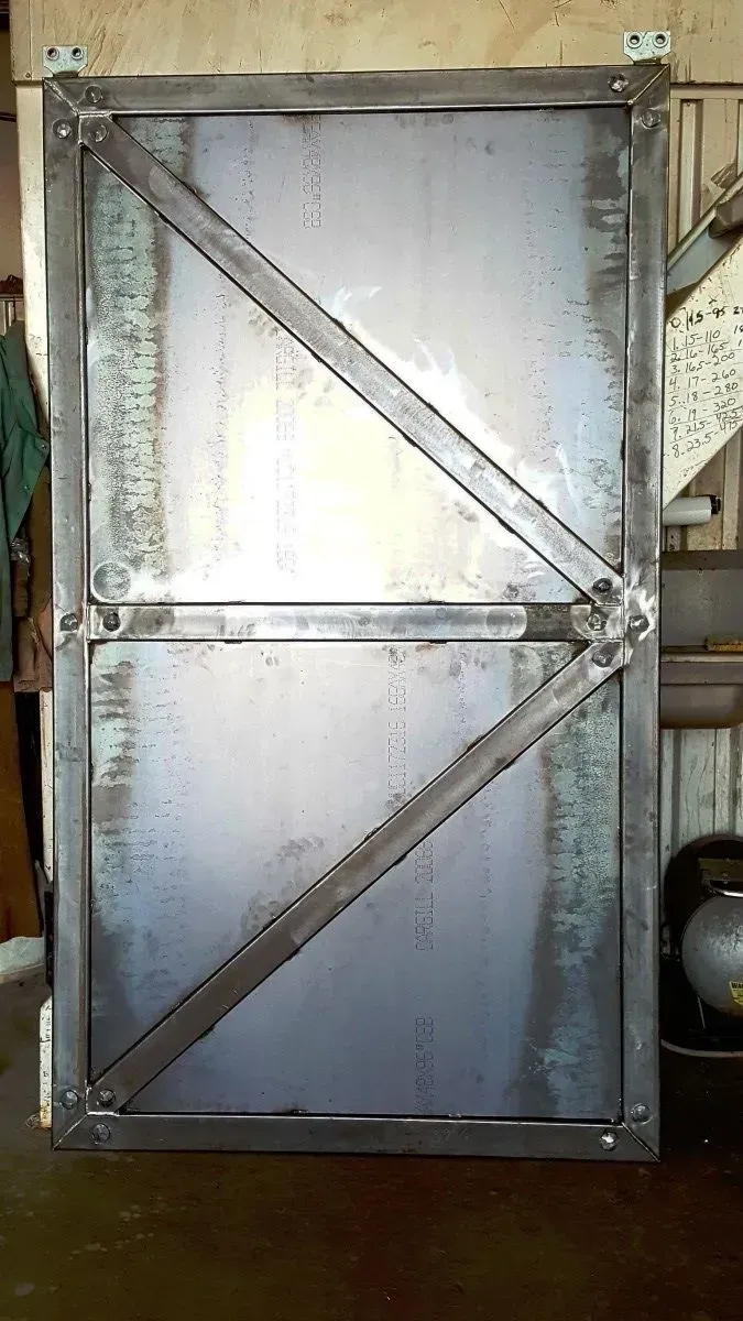 Metal industrial gate with diagonal braces and a silver panel in a workshop setting