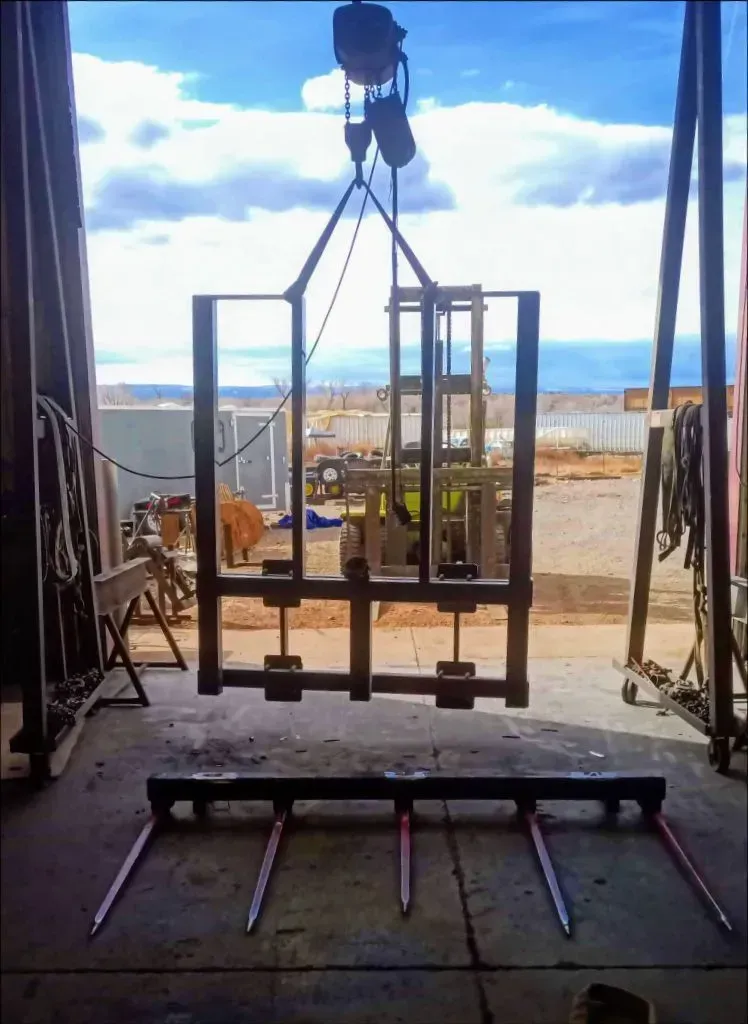 Industrial frame suspended by crane inside a workshop doorway, with bright sky and ocean visible beyond.