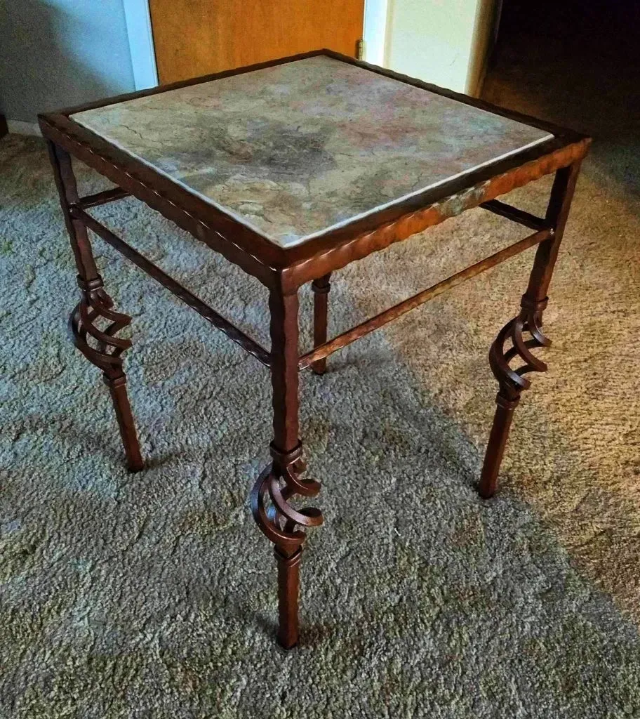 Small wooden side table with a square marble top and carved legs on a carpeted floor.